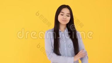 黄色背景的年轻亚洲女孩微笑着看着相机。 蓝色衬衫